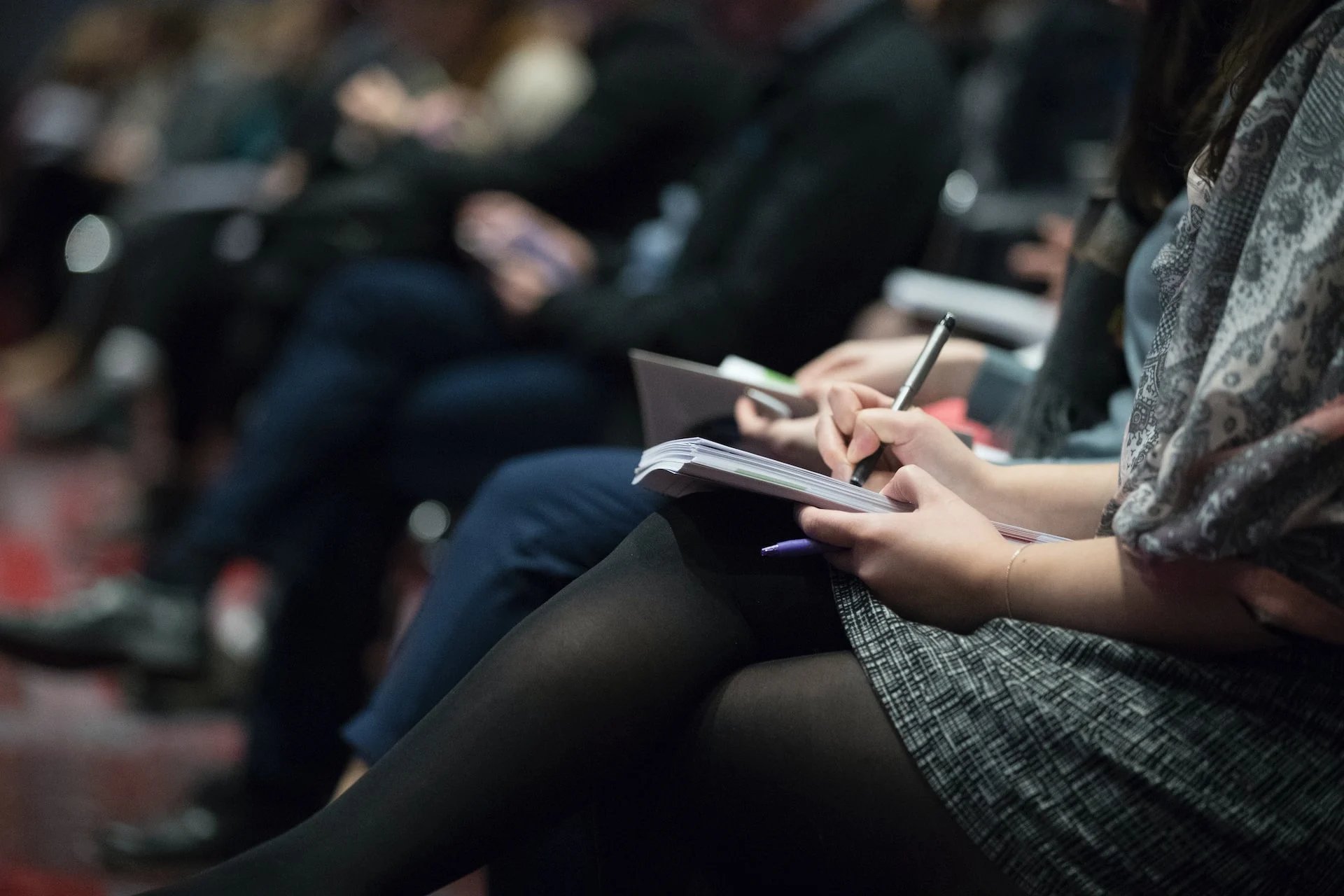 A woman sitting in a class writing notes in a notepad. 