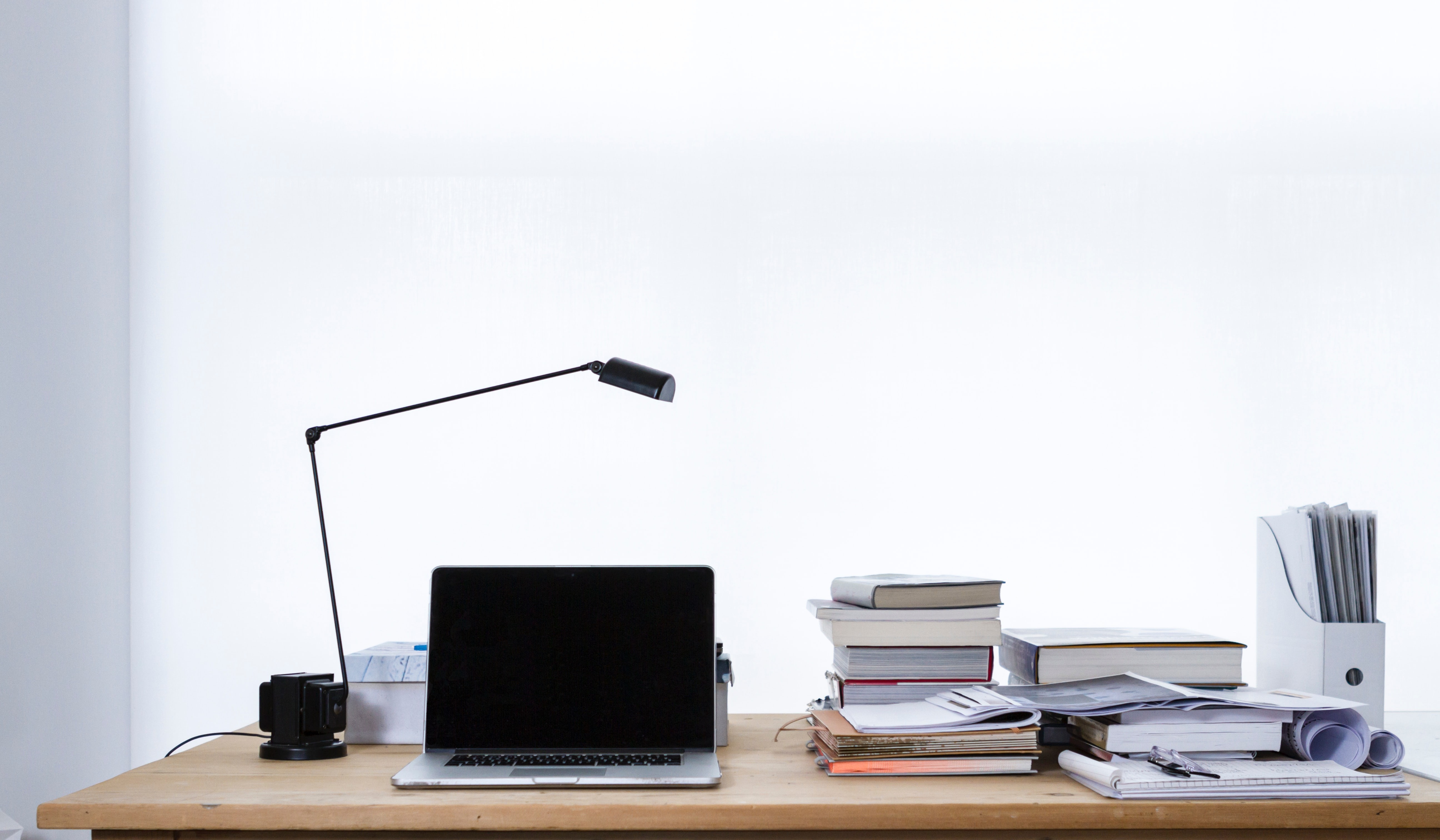 a desk with a laptop, lamp, and stacks of books and papers