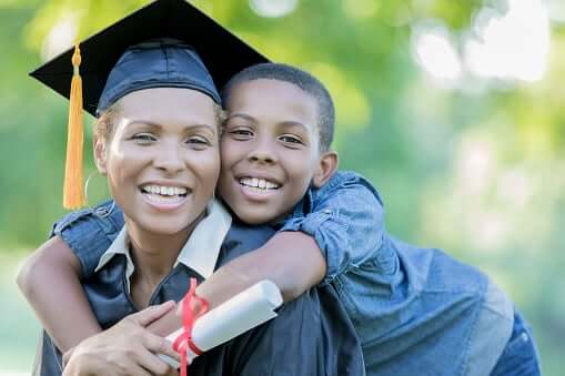 A mom and son hugging while the mom is holding a scroll and wearing a graduation cap.