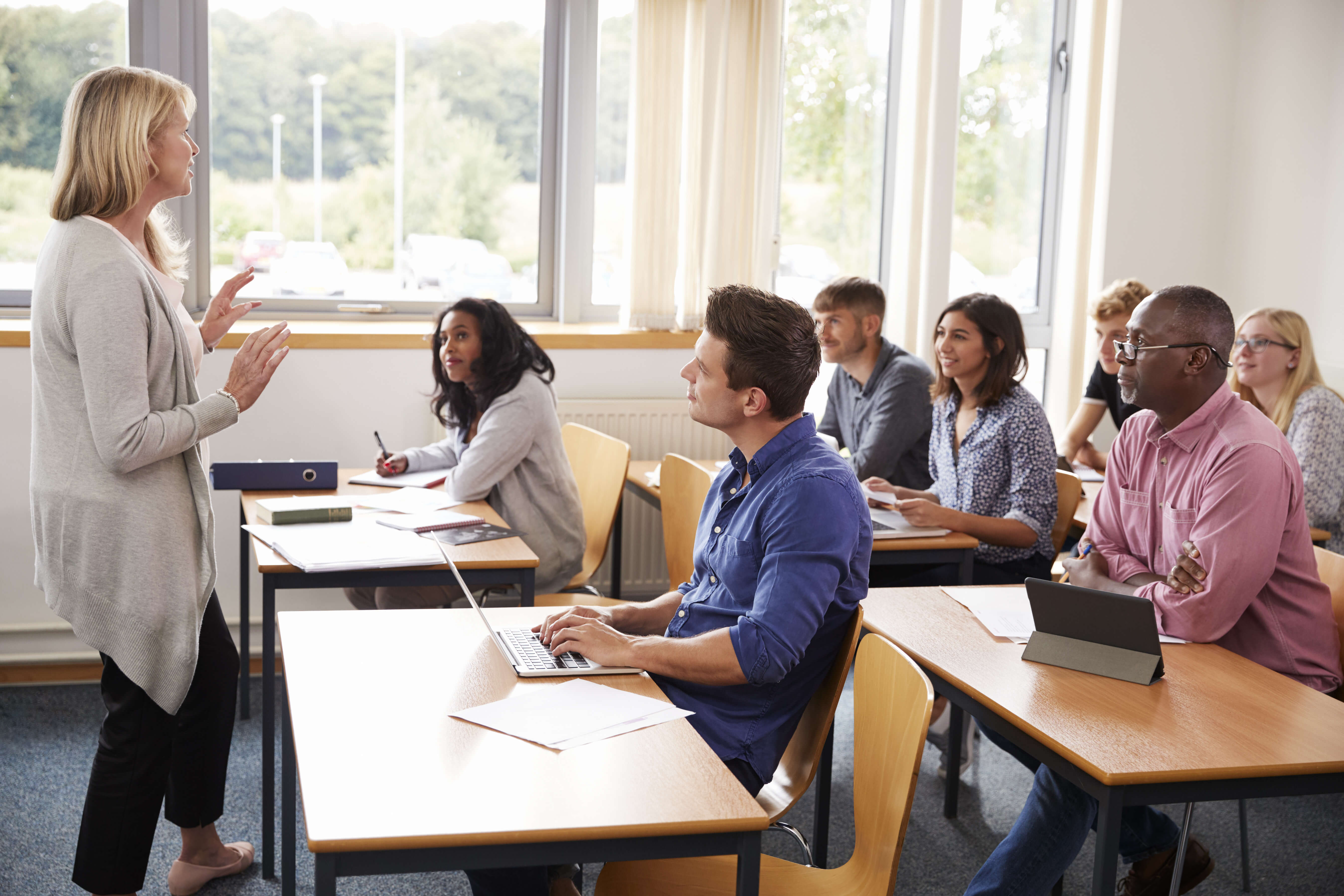 A group of adults sitting in a classroom looking at a teacher. 