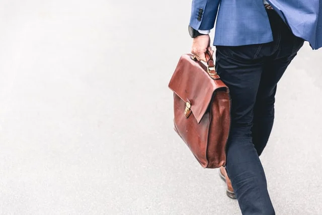 A person walking holding a brown briefcase. 