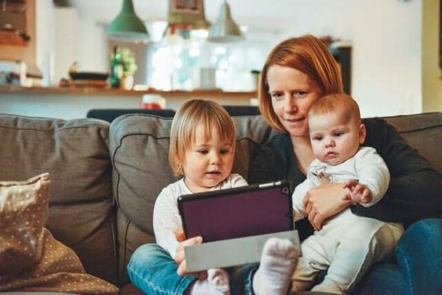 A mom holding her two babies on a couch. 